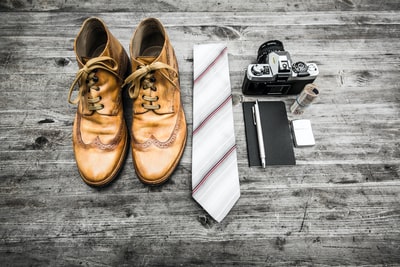 一双棕色皮靴，领带旁，钢笔、笔记本和MILC相机旁